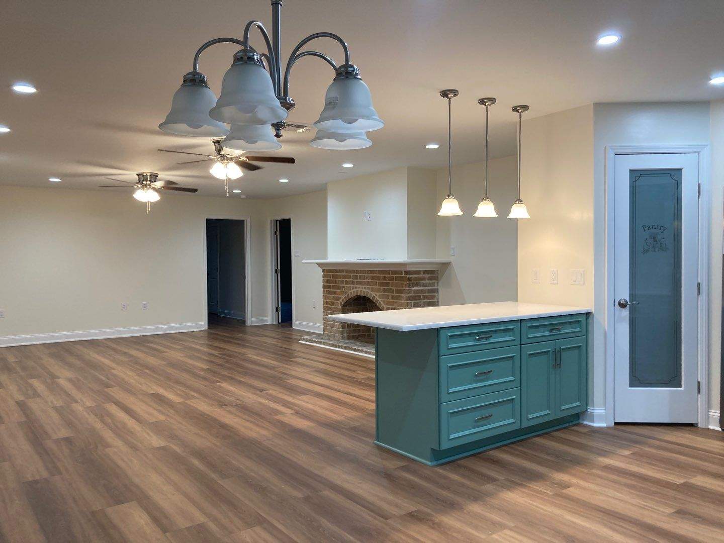 The great room looking toward the kitchen island and frosted-glass pantry door, with a chandelier and ceiling fan installed.