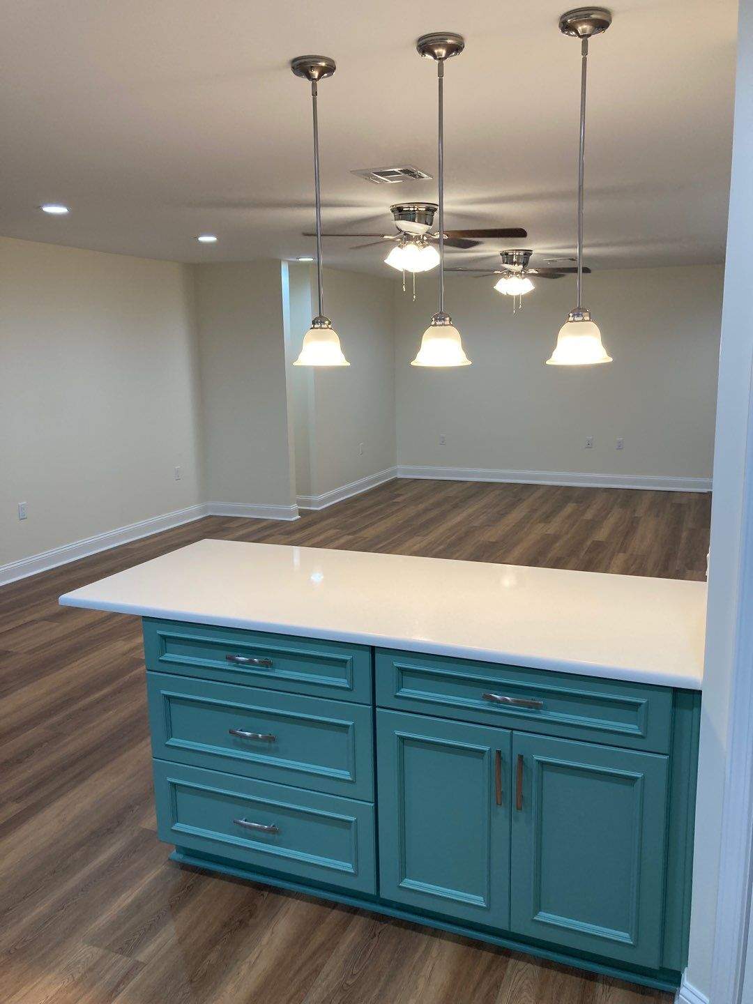 The kitchen island in white quartz and sage green, with the dining area and pendant lighting behind it.