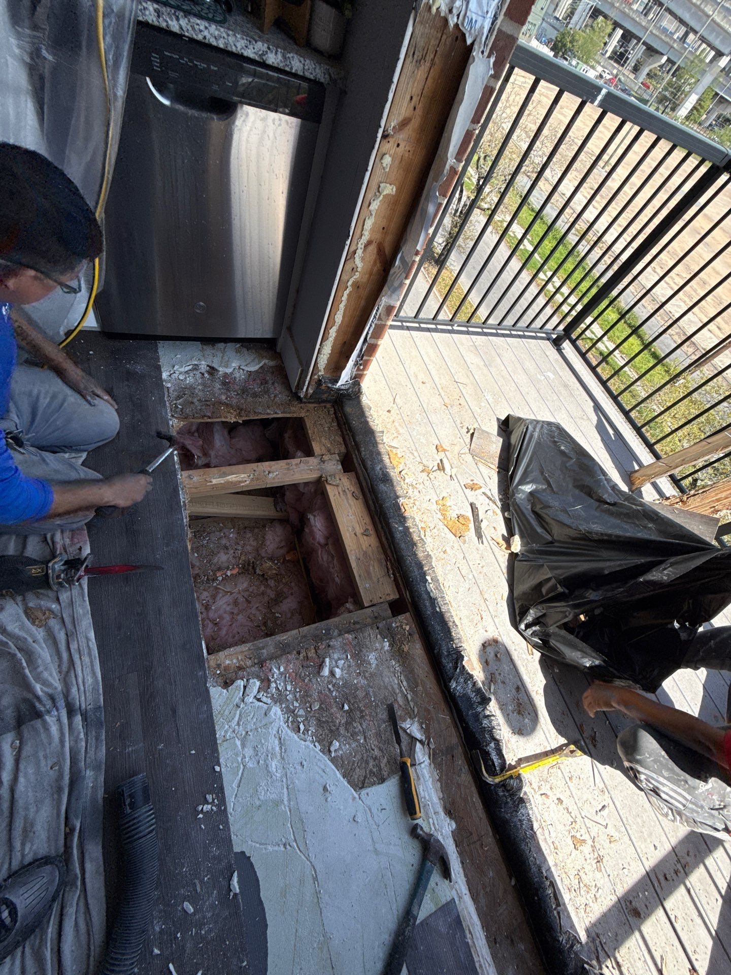 Interior flooring removed adjacent to the balcony entrance, exposing floor framing and insulation for repairs