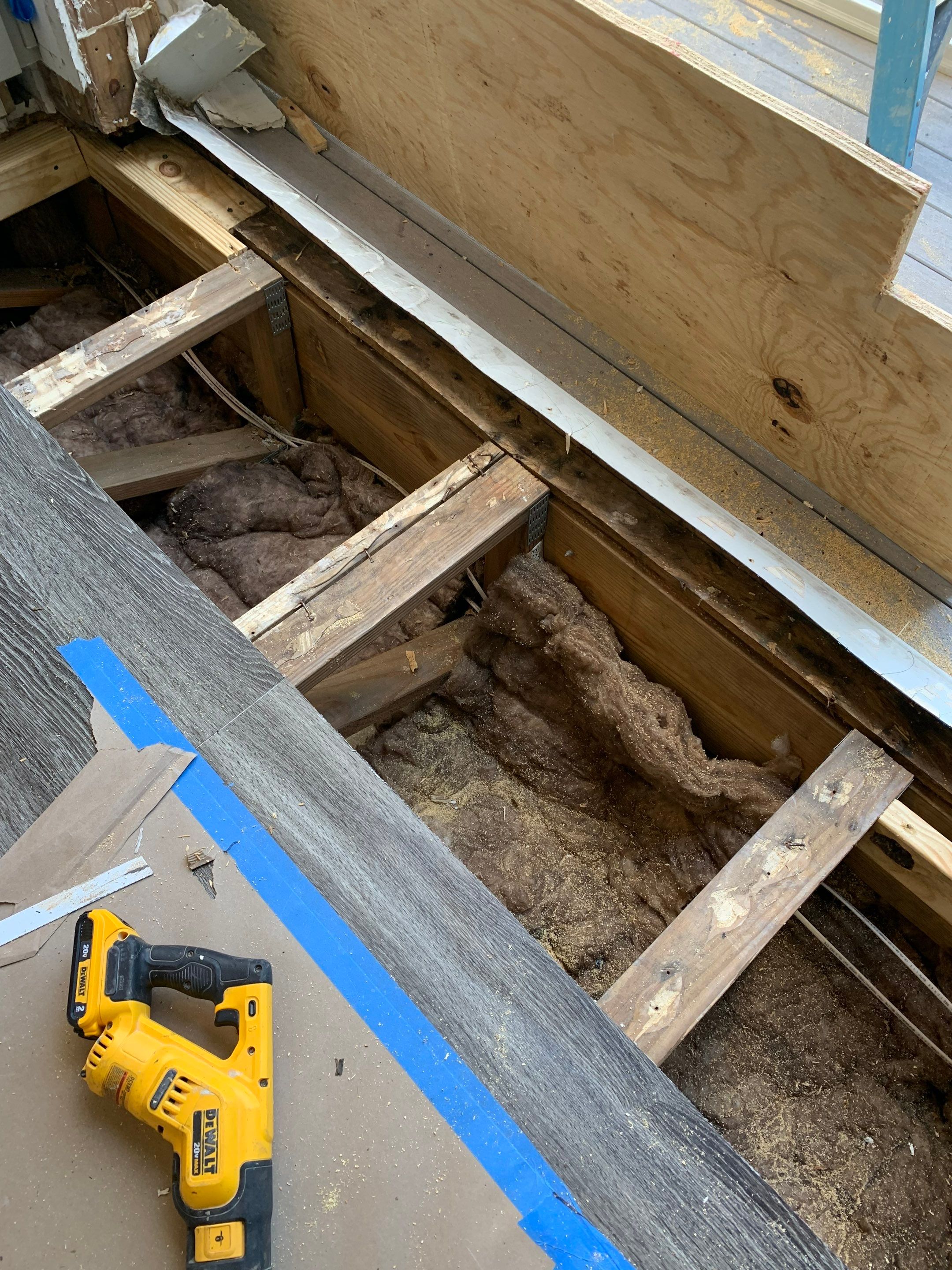 Exposed floor joists and insulation beneath the doorway following removal of damaged subfloor materials.