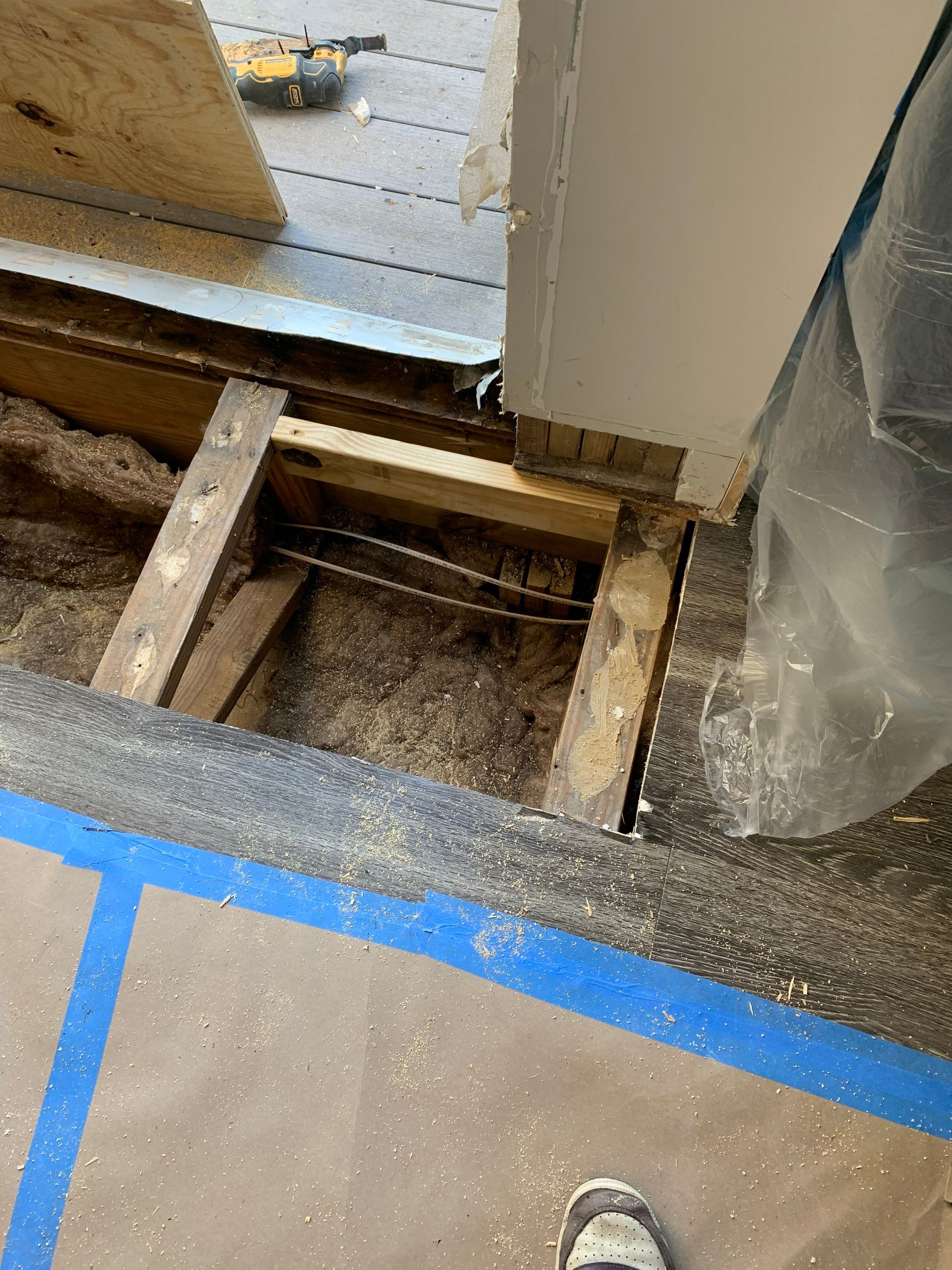 Subfloor opened beside the balcony threshold to inspect framing and underlying conditions.