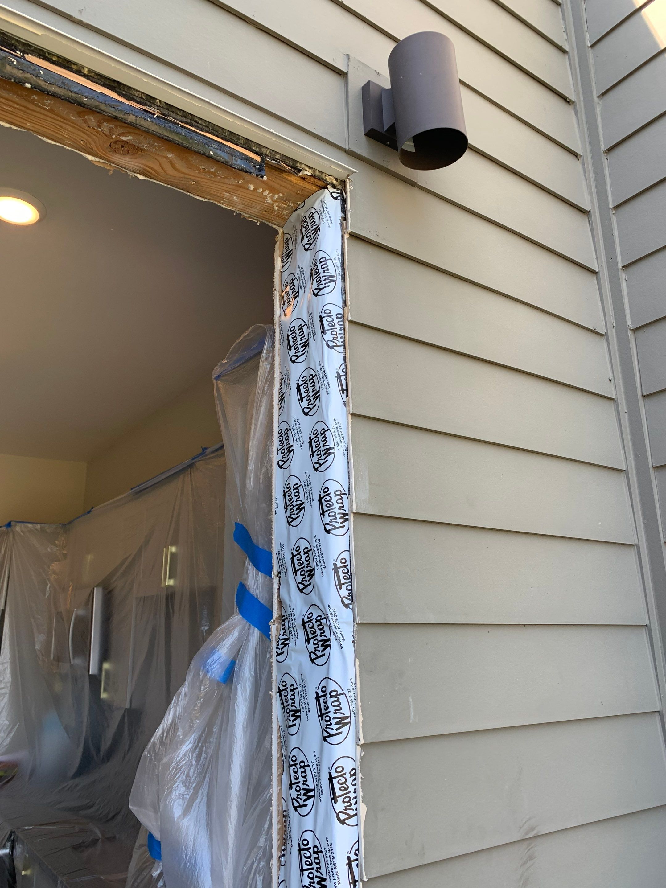 Exterior doorway framing with weather barrier installed along the jamb beneath the existing light fixture.