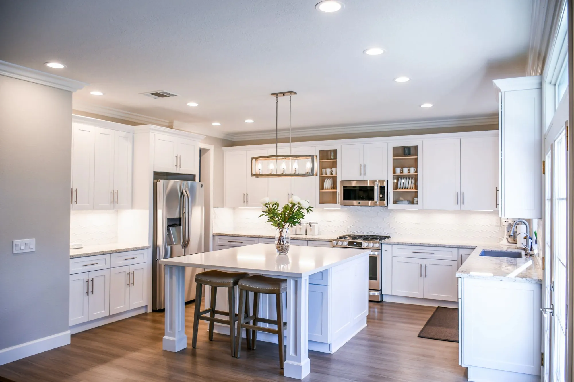 Modern white kitchen with island, stainless steel appliances, and wooden stools.