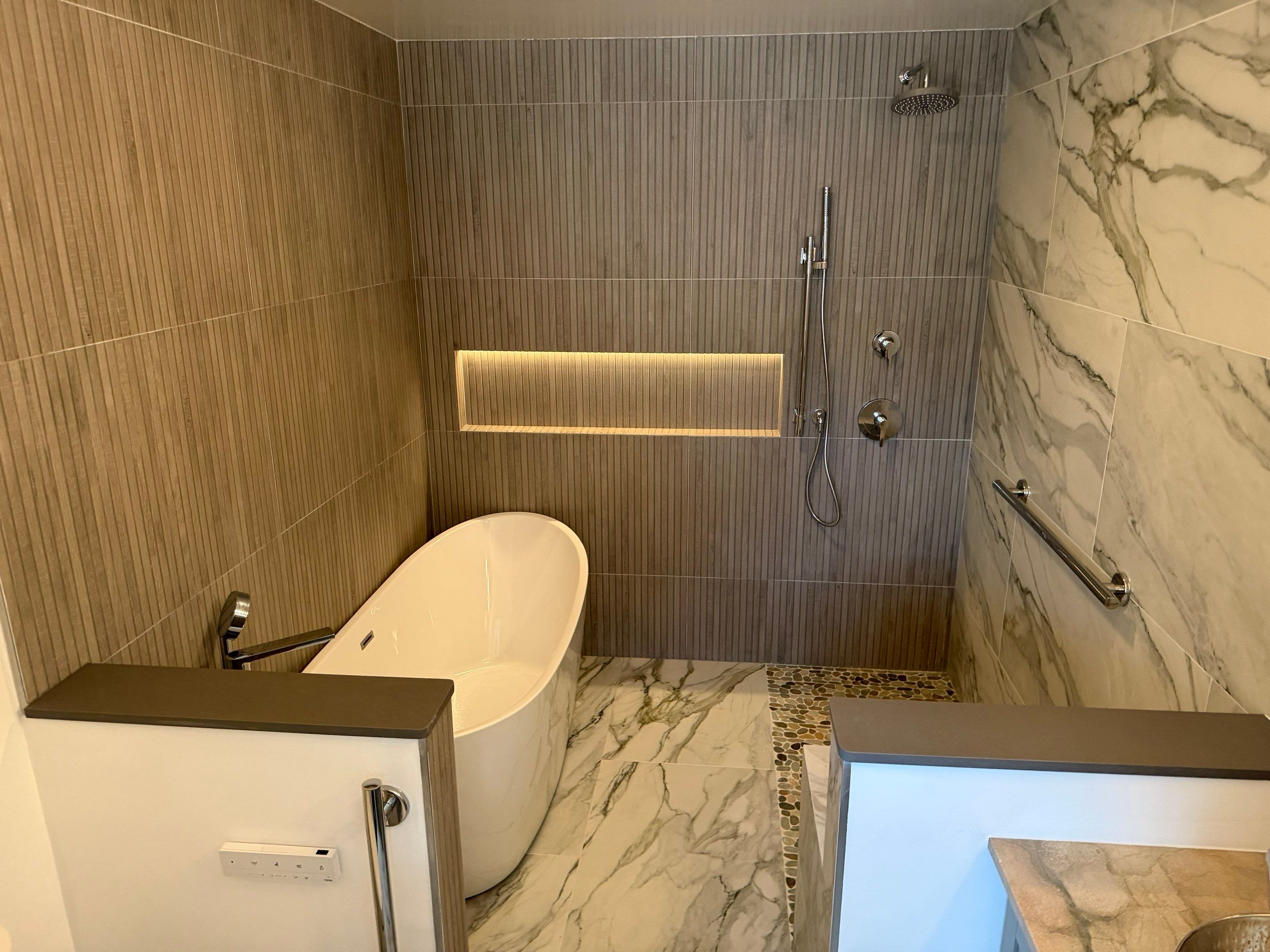 Modern bathroom featuring a freestanding soaking tub, walk-in shower, illuminated niche, marble-look tile, and grab bars.