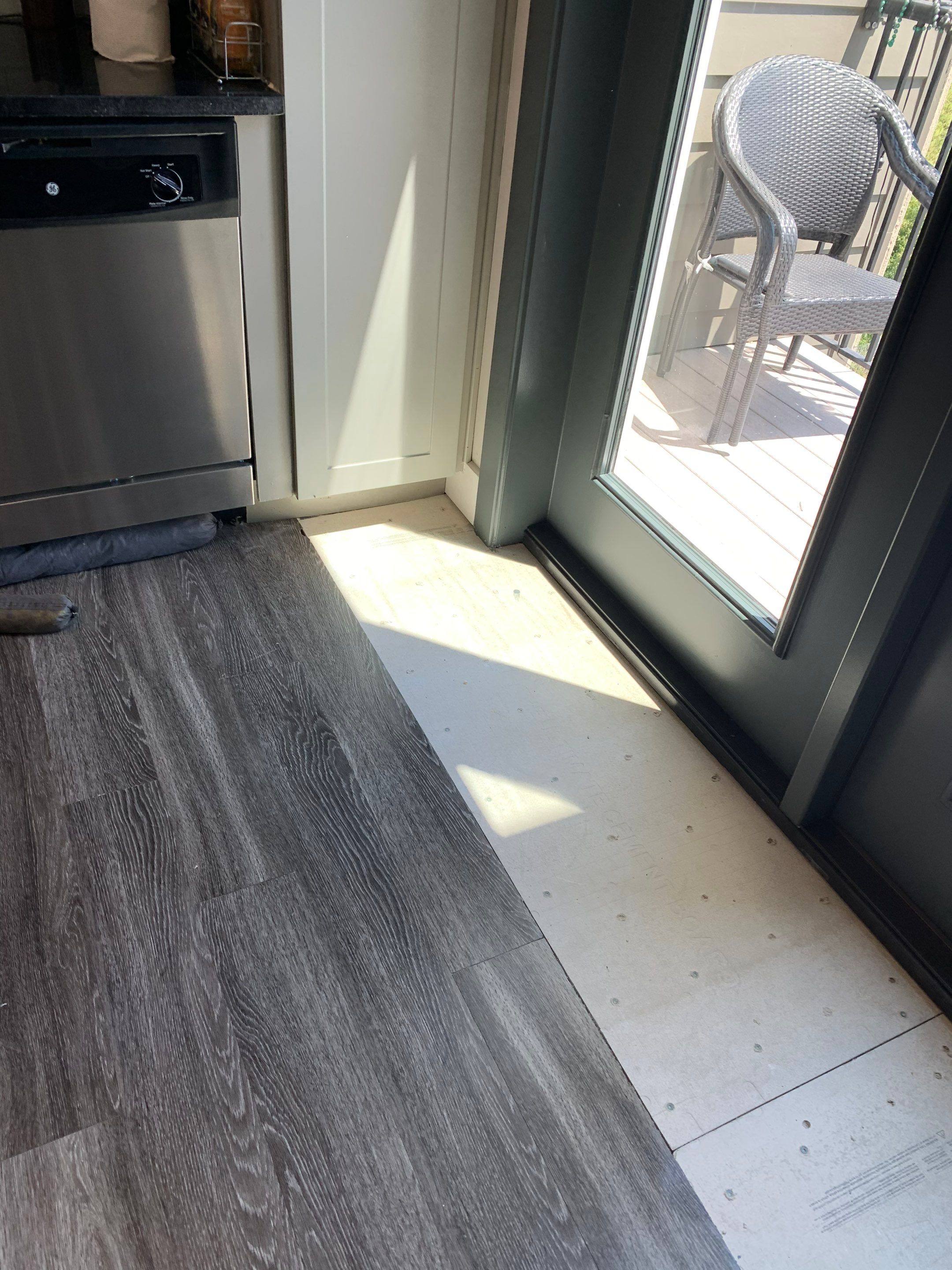 Interior flooring repair area beside the newly installed balcony door, showing replacement underlayment before flooring installation.