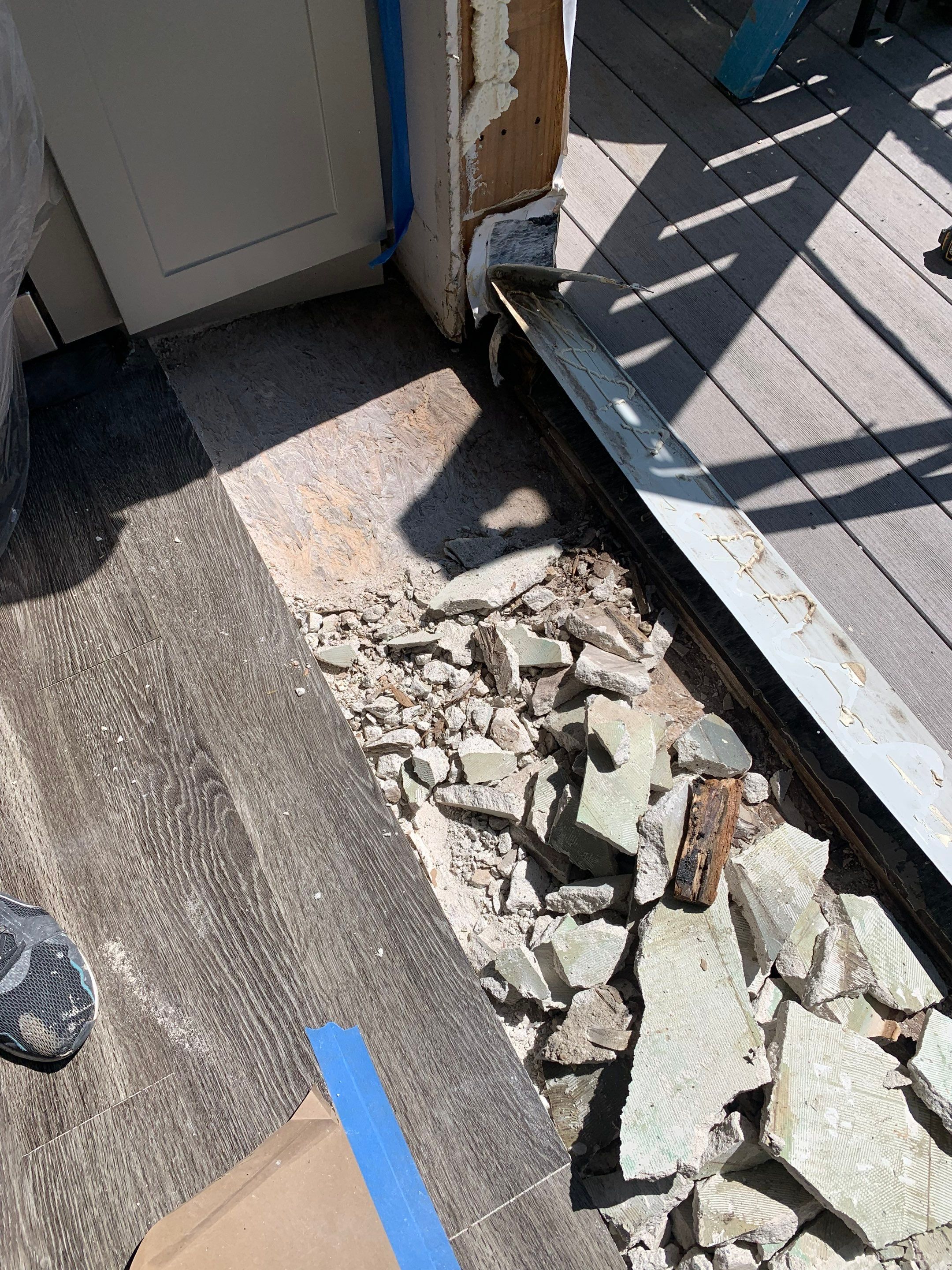 Damaged flooring and underlayment removed near the balcony threshold to access the underlying subfloor.